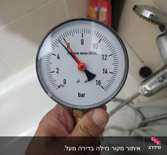 מד לחץ מים מוחזק ביד ליד ברז במקלחת